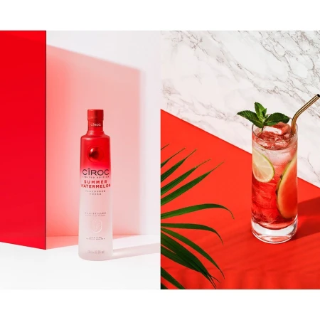 Studio shot of a Ciroc Summer Watermelon vodka bottle and a highball glass with watermelon cocktail against colorful studio background.