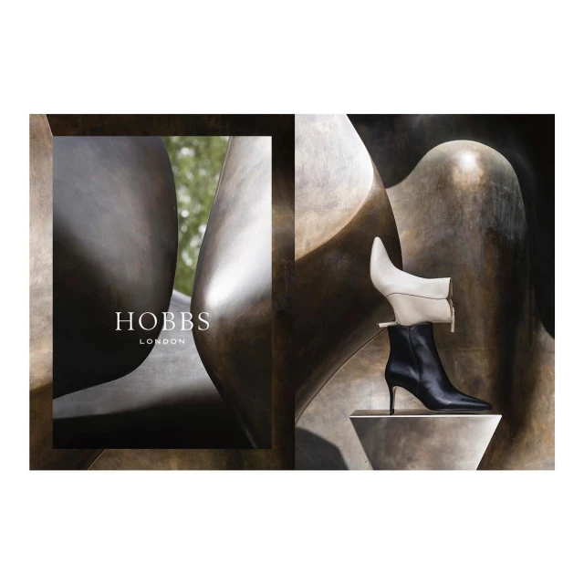 Fashion editorial shot of two leather heeled boots, one white and one black, displayed against a brown abstract sculptural backdrop.
