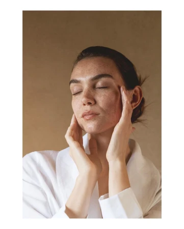 Close-up shot of a serene woman with closed eyes, gently touching her face against a neutral background, highlighting skincare and wellness.
