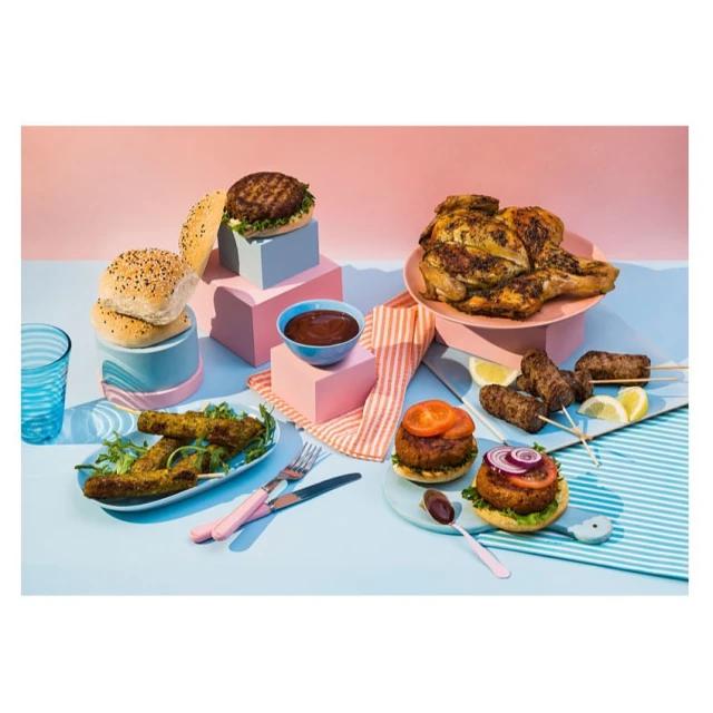 Eye-level shot of an assortment of grilled dishes on a blue surface with pink geometric risers, a refreshing, appetizing aesthetic.