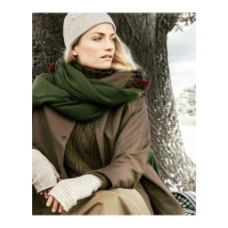 Woman wearing a knit beanie, green scarf, and brown coat outdoors against a large tree trunk background.