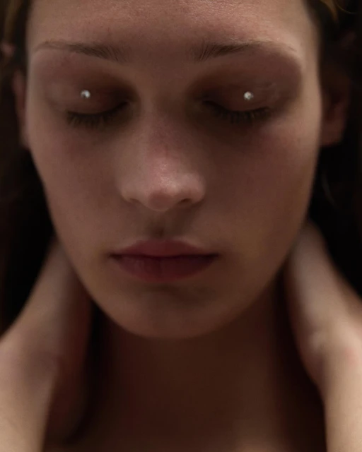 Close-up portrait of a woman with closed eyes and eye piercings, focusing on her facial features and neutral expression, indoors.