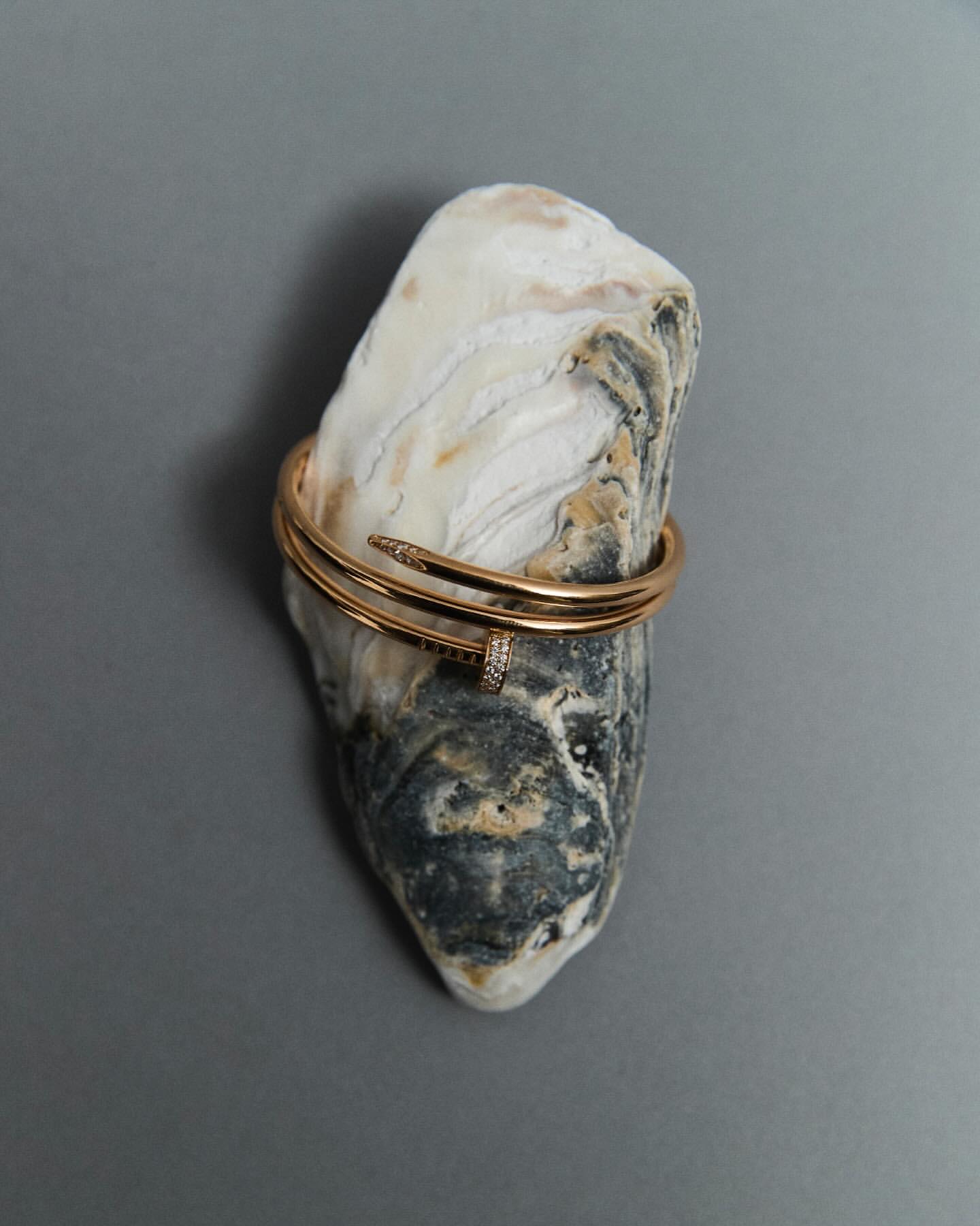 Close-up of a gold nail bracelet on a textured rock, studio shot, emphasizing jewelry and object photography.