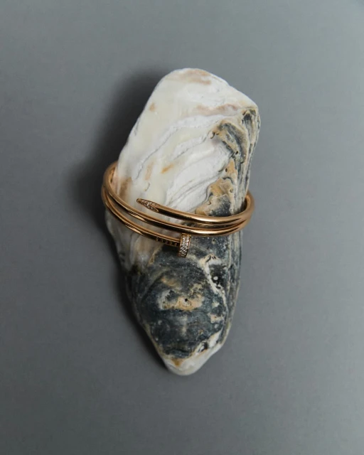 Close-up of a gold nail bracelet on a textured rock, studio shot, emphasizing jewelry and object photography.