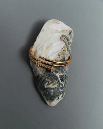 Close-up of a gold nail bracelet on a textured rock, studio shot, emphasizing jewelry and object photography.