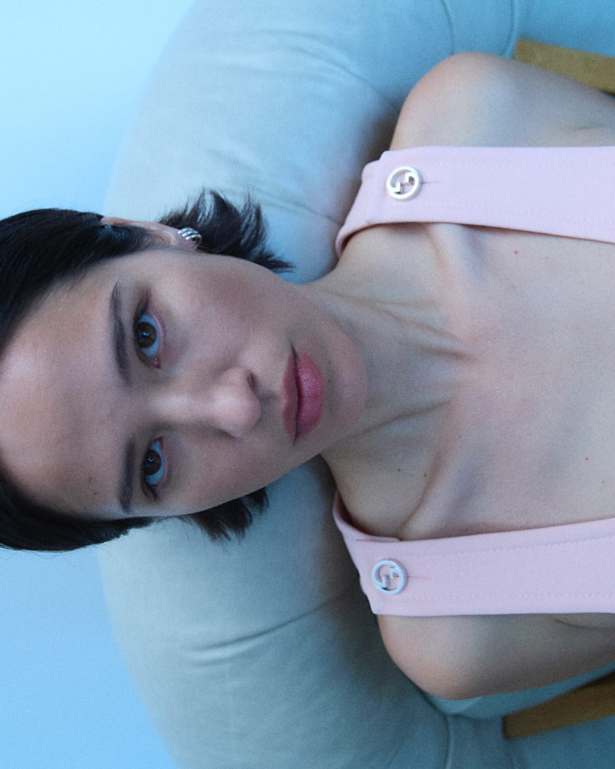 Close-up studio portrait of a young adult female wearing a light pink top with shoulder straps, looking directly at the camera.