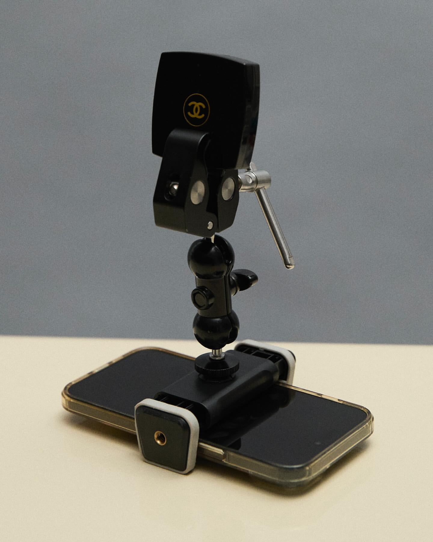 Close-up studio shot of black smartphone attached to an adjustable metal tripod stand with a Chanel logo on the phone's back.