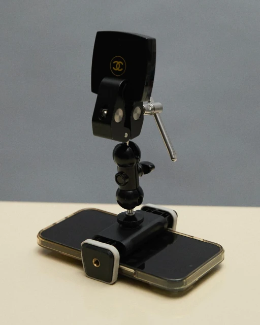 Close-up studio shot of black smartphone attached to an adjustable metal tripod stand with a Chanel logo on the phone's back.