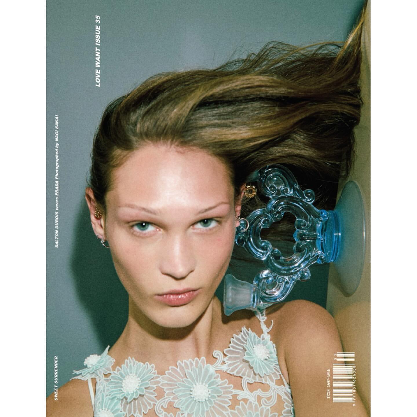 Close-up fashion magazine cover shot of a fair-skinned adult woman with light brown hair, wearing a floral top and blue decorative object.