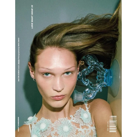 Close-up fashion magazine cover shot of a fair-skinned adult woman with light brown hair, wearing a floral top and blue decorative object.