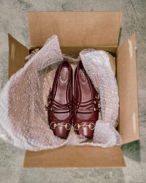 Pair of Gucci ballerina shoes displayed in a cardboard box with bubble wrap packaging, showcased indoors, emphasizing brand and product details.