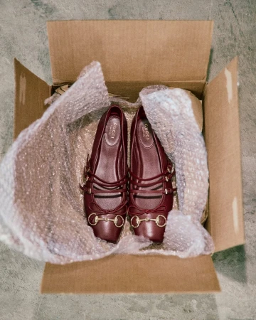 Pair of Gucci ballerina shoes displayed in a cardboard box with bubble wrap packaging, showcased indoors, emphasizing brand and product details.