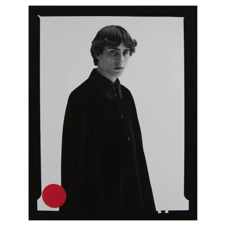 Portrait of a slender adult male model in a black coat, with dark hair and a red circle detail on a monochrome background in a studio.