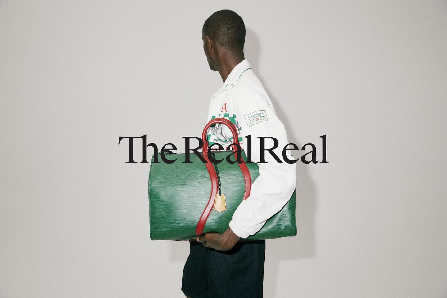 A person carries a green leather duffel bag with red straps in a studio shot with simple background, featuring the 'The RealReal' logo.