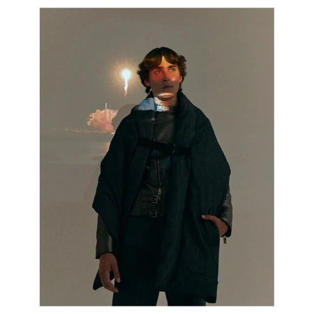 Young man poses in a stylish black outfit, with a space shuttle launch projected in the background, creating a modern, artistic portrait.