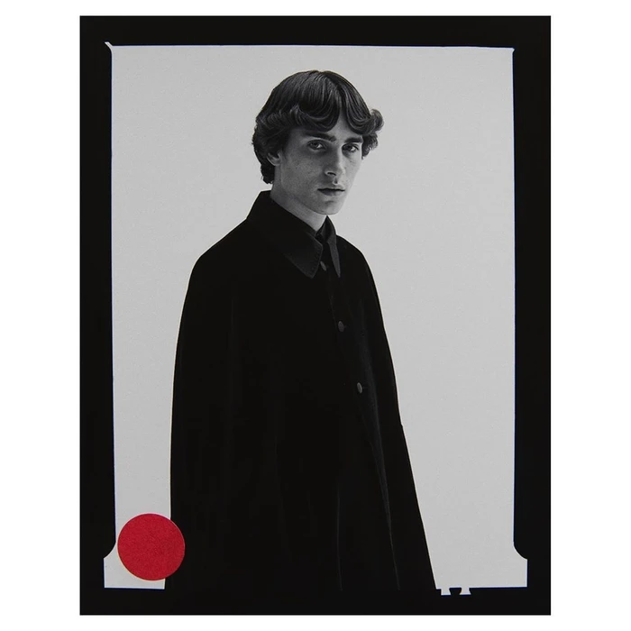 Black and white editorial portrait of a young man wearing a dark buttoned coat against a light background by Nagi Sakai