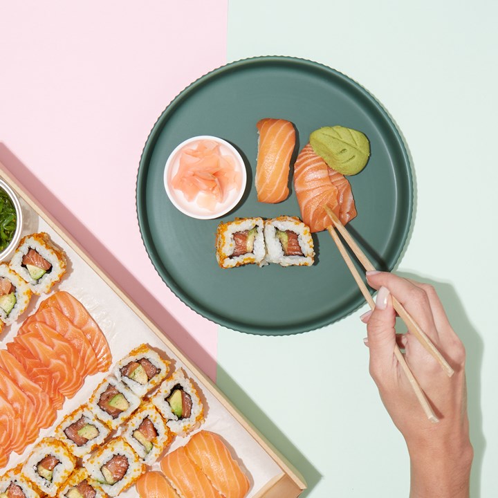 Overhead shot of sushi assortment, including rolls, sashimi, and nigiri, arranged on a green plate and in a wooden box.