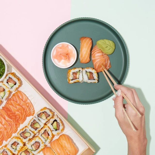 Overhead shot of sushi assortment, including rolls, sashimi, and nigiri, arranged on a green plate and in a wooden box. 