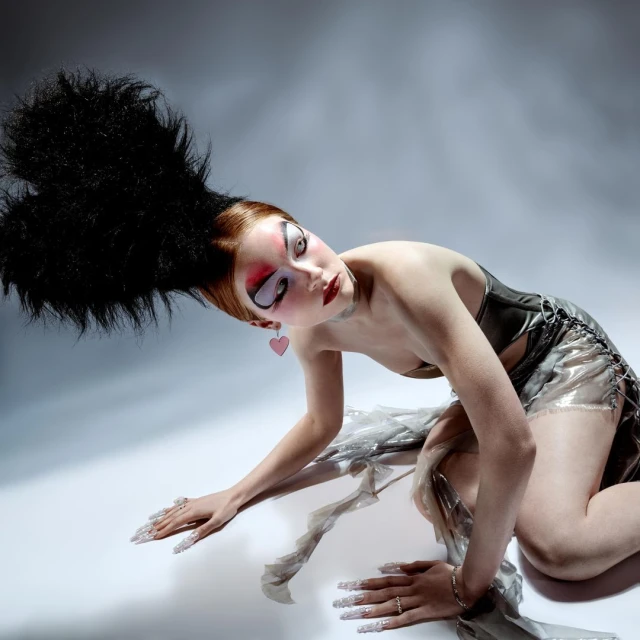 Dramatic fashion portrait of a model with high-fashion goth style, extreme makeup, a silver corset, and a distinctive high hairpiece. 