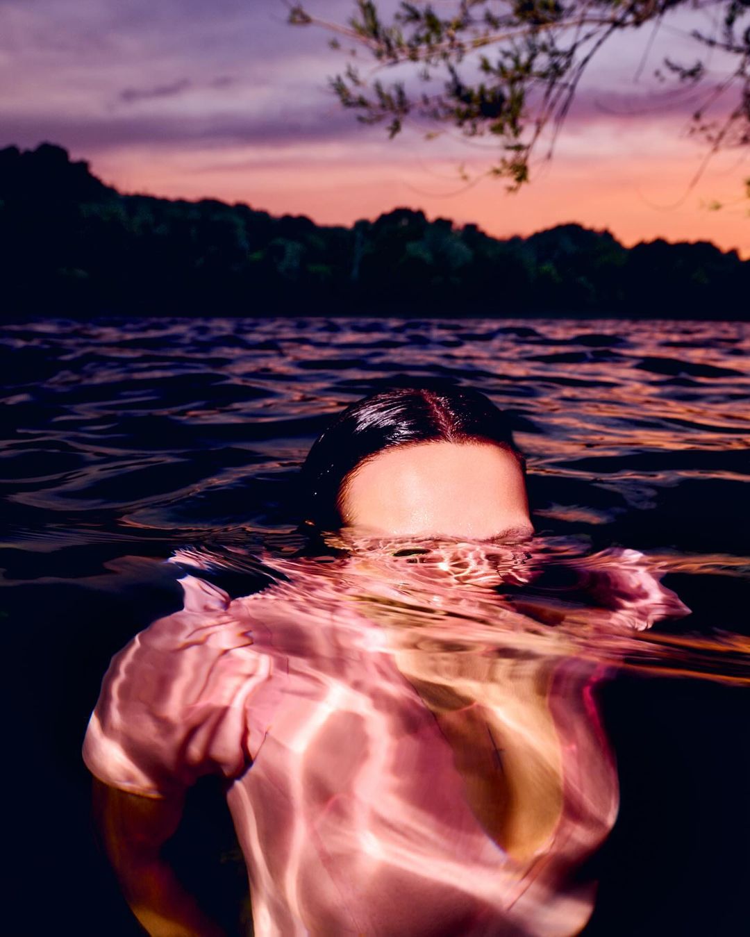 Woman swimming in a lake at sunset, with ripples in the water and trees in the background, creating a serene and natural scene.