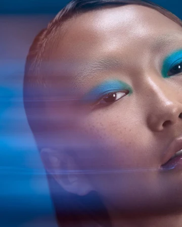 Close-up beauty portrait of a woman with vibrant blue eyeshadow and motion blur streaks across the frame, photographed by Nadia Correia.
