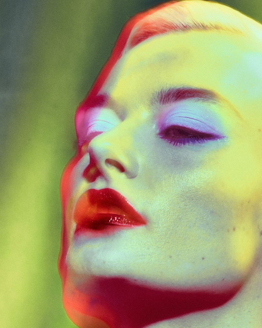 Close-up portrait of a woman with red lips and purple eyeshadow under colored lighting by Nadia Correia