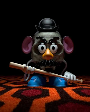 Creepy Mr. Potato Head toy on a patterned carpet and a black background. A wooden stick accentuates the unsettling scene.