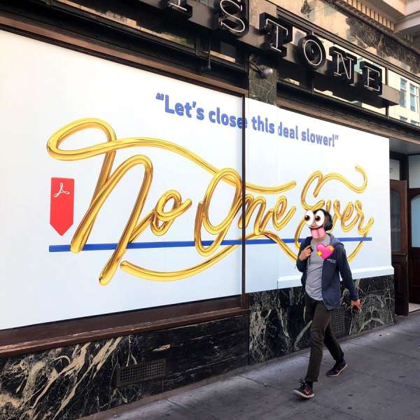 Street-level view showcases a person walking past a storefront with a large advertisement featuring golden script and a red vector graphic.