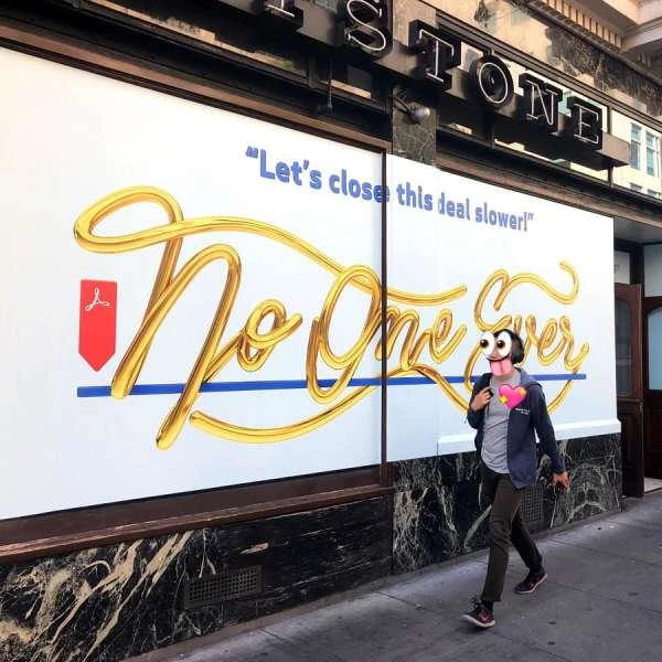 Street-level view showcases a person walking past a storefront with a large advertisement featuring golden script and a red vector graphic.