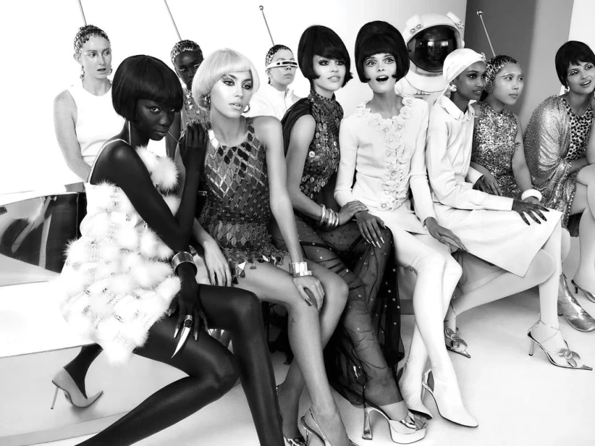 Group of diverse fashion models in retro-futuristic attire and hairstyles, seated in a studio setting, showcasing vintage-inspired looks.