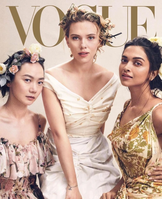 Vogue cover featuring three women with floral headpieces. The woman in the center wears an off-the-shoulder white dress; the women on either side wear floral print dresses.