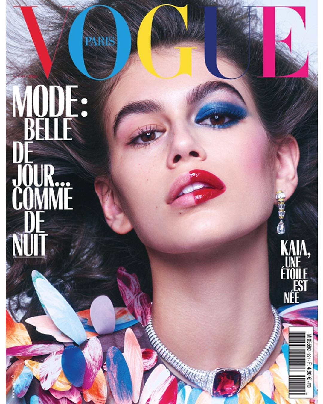 Vogue magazine cover featuring a model with dramatic makeup, statement jewelry, and colorful floral accents for a beauty and fashion editorial.