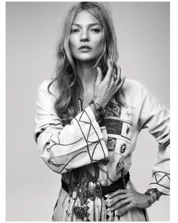 Monochrome portrait of a fashionable adult woman with long blond hair, wearing an embroidered tunic and multiple pieces of jewelry.