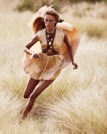 Model in gold pleated dress running through tall grassland captured by photographer Mikael Jansson
