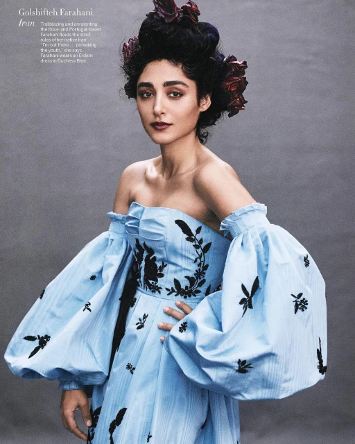 Elegant woman in a light blue off-the-shoulder dress with black floral embroidery and elaborate hairstyle adorned with flowers, portrait style.