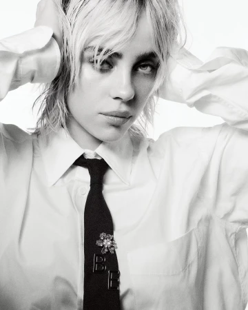 Black-and-white portrait of Billie Eilish wearing a white collared shirt and black tie with her hands behind her head.
