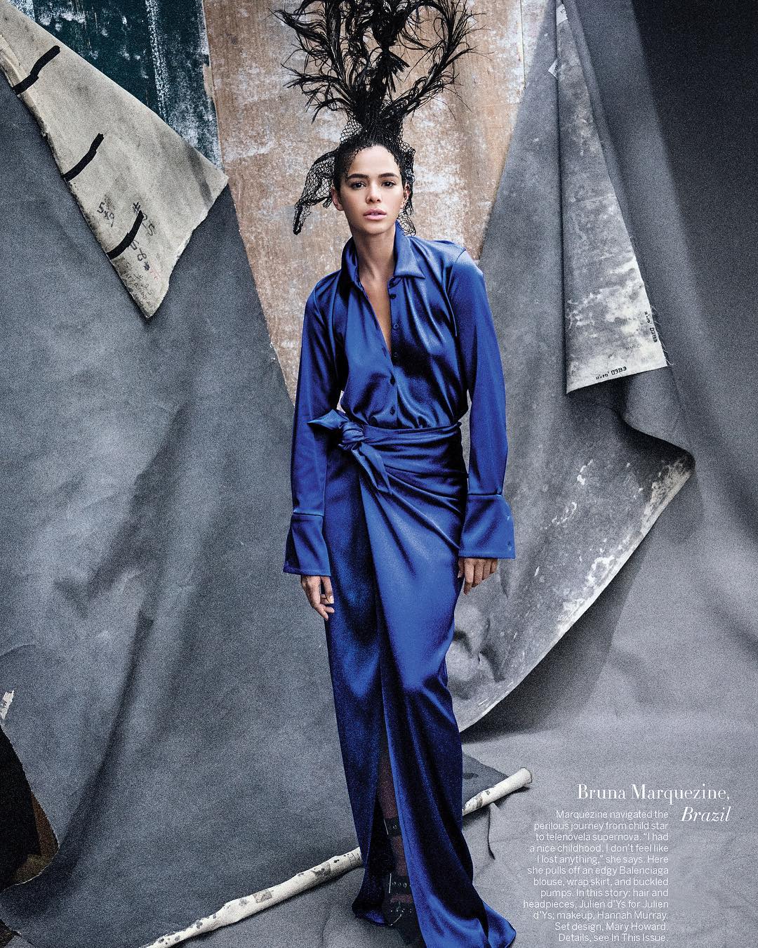 Fashion shot of woman in cobalt-blue dress with dramatic headdress posing in front of a textured grey studio backdrop with birch branches.