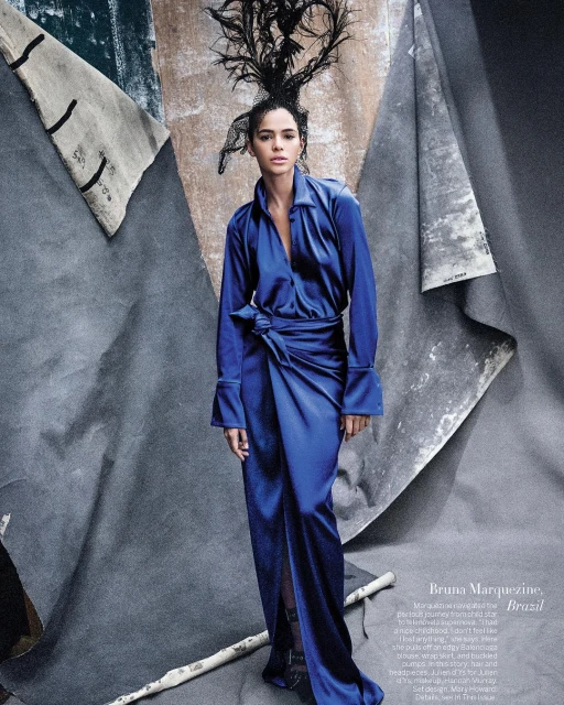 Fashion shot of woman in cobalt-blue dress with dramatic headdress posing in front of a textured grey studio backdrop with birch branches.