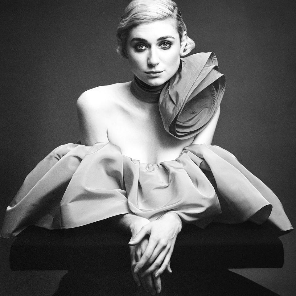 Monochromatic portrait of an adult female model with a short blonde hairstyle, wearing a sculpted peach dress with expressive ruffles.