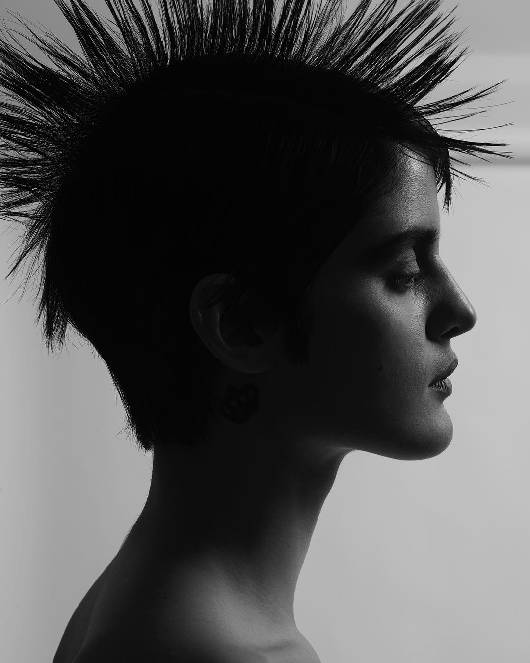 Monochrome portrait of a young adult woman in profile, showcasing a short hairstyle with spiky strands and a neutral facial expression.