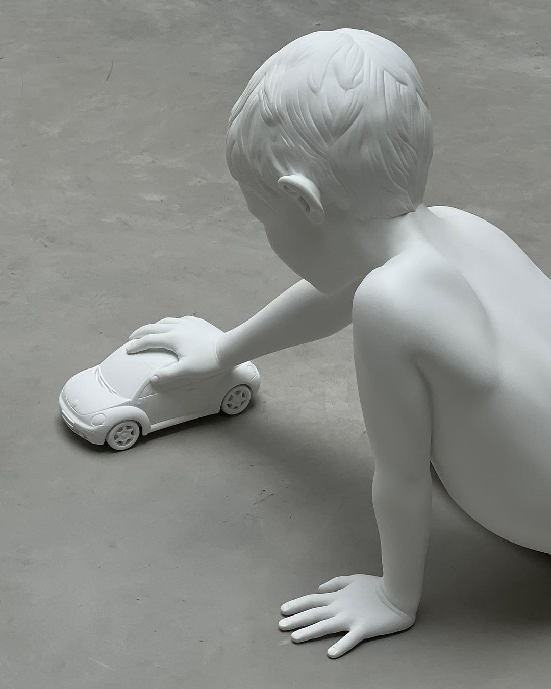 Monochromatic art still life of a child statue playing with a car toy in a modern setting, shot with neutral, soft lighting.
