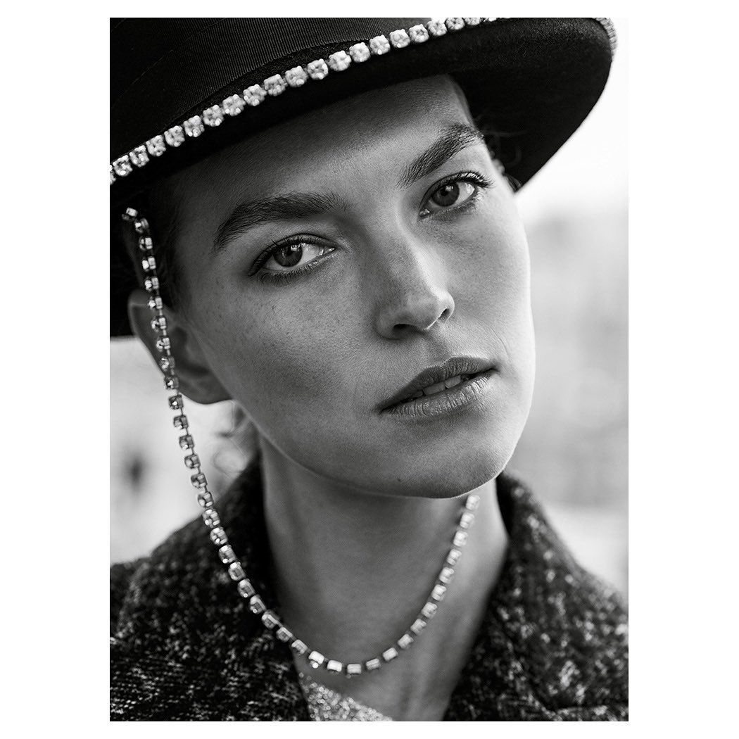 Monochrome portrait of a woman with a hat, wearing a rhinestone chain and necklace, with a serious expression, shot in medium close-up.