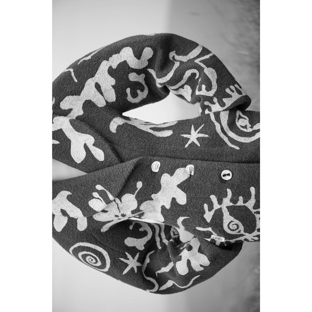 Close-up black and white shot of a folded fabric scarf with a white abstract pattern, featuring stars and spiral designs.