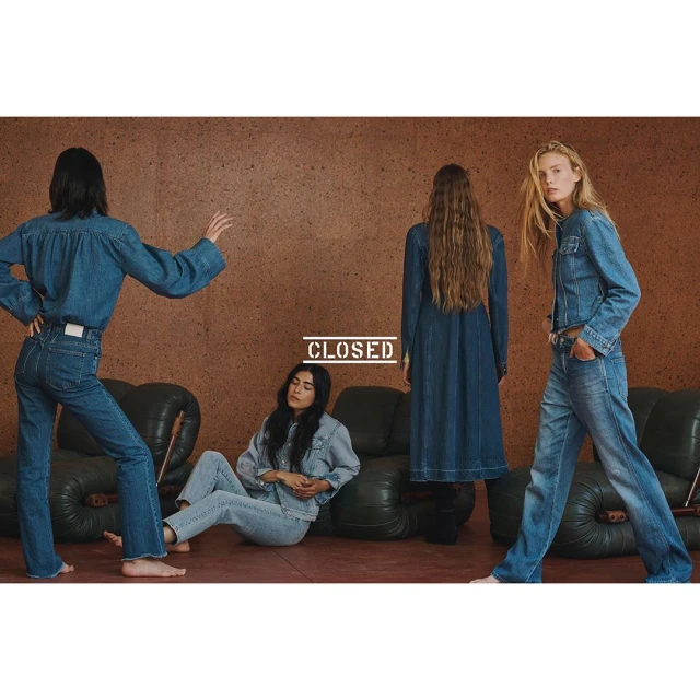 Four women in denim outfits pose in front of a cork wall and dark green sofas, showcasing a fashion editorial with a vintage mood.