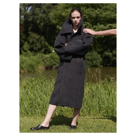 Model standing outdoors in a dark grey plaid coat with arms crossed, photographed by Mel Karch.
