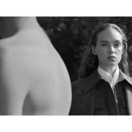 Monochrome portrait of a woman in a collared shirt and jacket with an out of focus bare torso in the foreground.