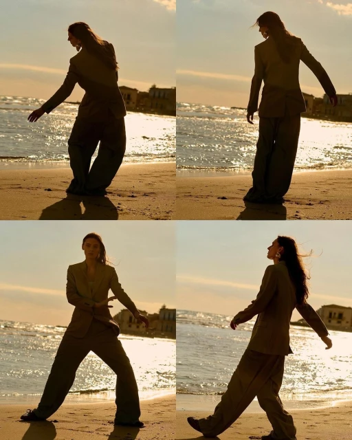 A person in a blazer and wide-legged trousers posing on a beach, the warm light creating a silhouette effect as they walk in the sand.
