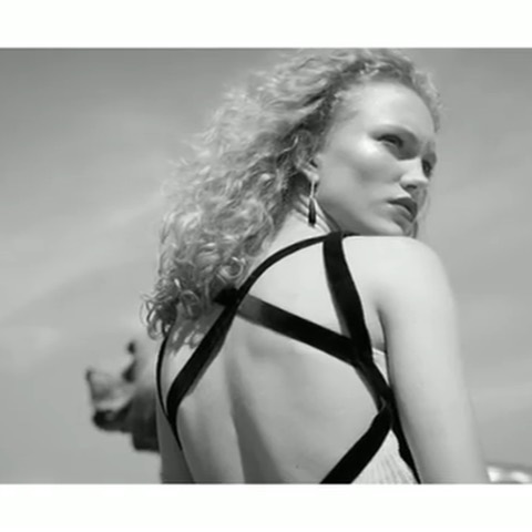 Black and white portrait of a curly-haired woman in black dress with open back, earrings and outdoor background with muted tones.