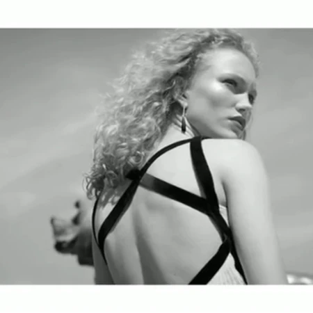 Monochrome portrait of a woman with curly blonde hair wearing a strappy dress, looking back over her shoulder outdoors