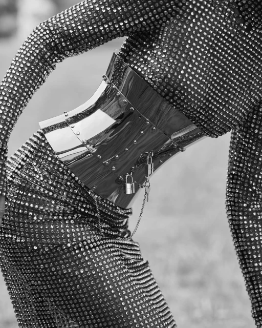 Person wearing a sparkling sequined bodysuit with a shiny metal corset and lock-and-key embellishments, standing outdoors in a fashion shot.